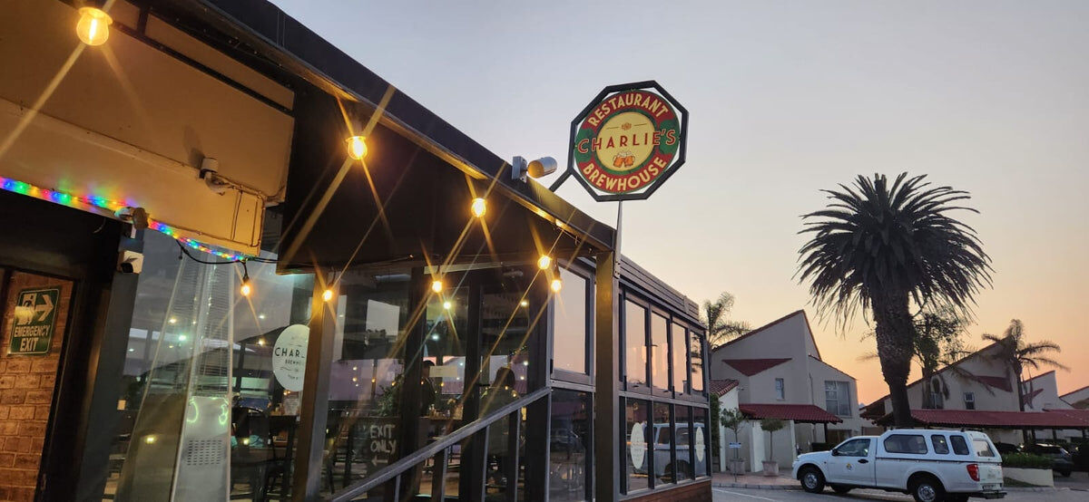 The Charlie's Brewhouse sign lit at sunset, with a palm tree behind